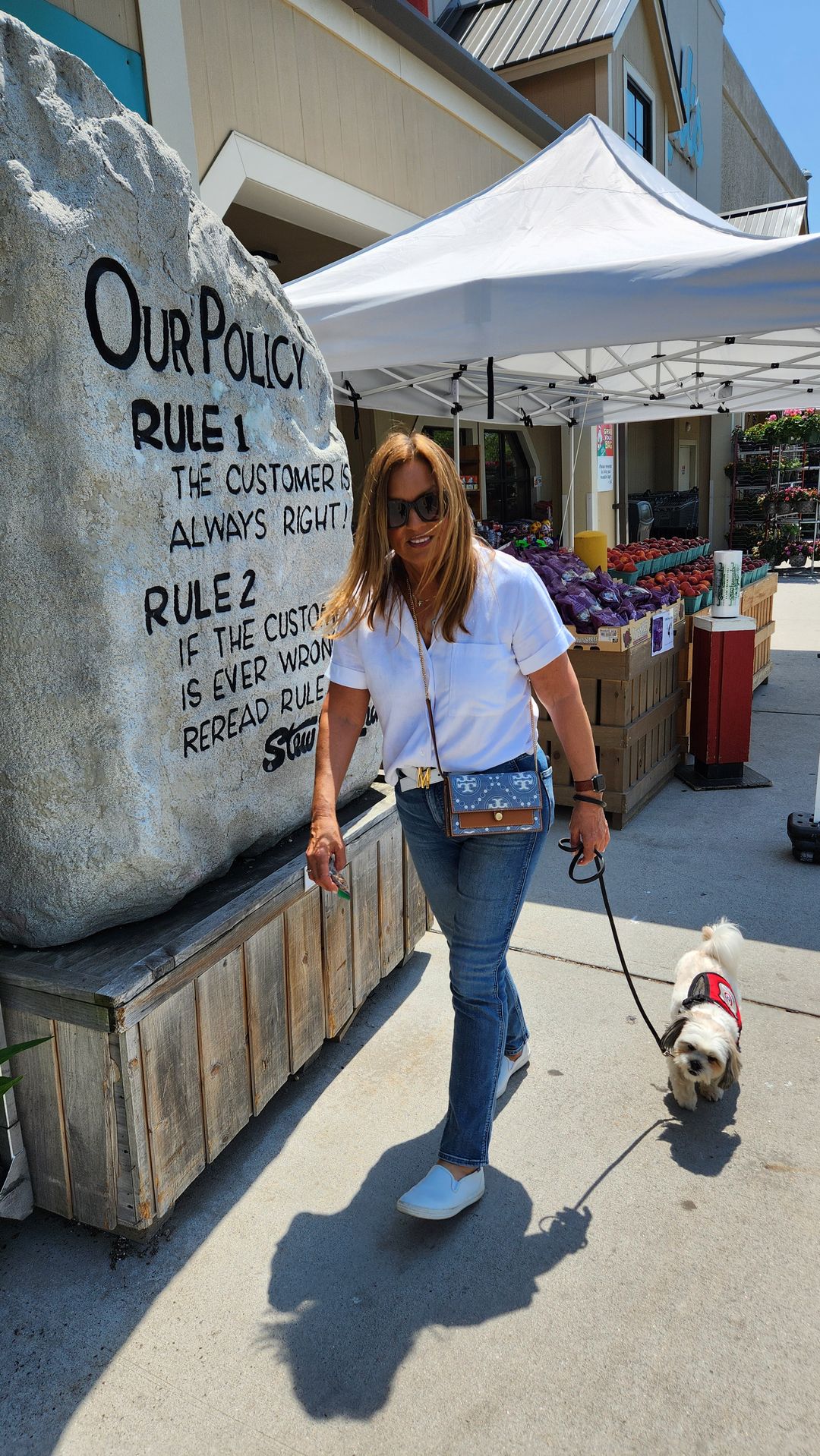 A small service dog in a red vest walking into Stew Leonard's on a loose leash beside its handler
